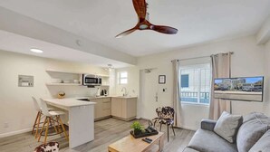 Eine moderne Wohnung mit Küche, Essbereich und Wohnzimmer. Sie verfügt über einen Deckenventilator, einen Fernseher und ein großes Fenster mit Vorhängen.