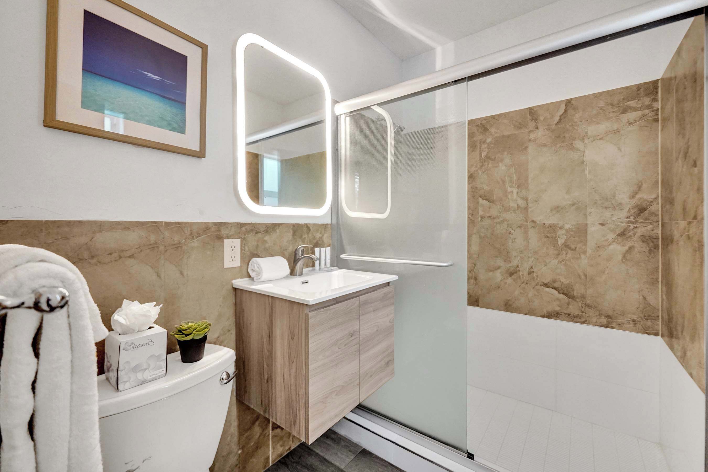 Un baño moderno con cabina de ducha de vidrio, un lavabo blanco y una pared revestida de mármol.