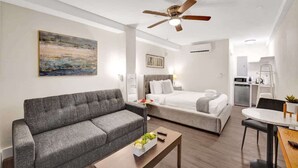 Moderni hotellihuone, jossa on harmaa sohva, sänky, ruokapöytä ja kattotuuletin.