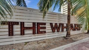 A sign with illuminated letters spelling "THE WHARF" against a white wall with horizontal lines.