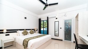 Habitación de hotel moderna con una cama grande, un escritorio, una silla, ventilador de techo, puerta con panel de vidrio y vistas al exterior.