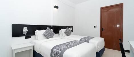 A modern hotel room with two beds, a white nightstand, a desk, and a wooden door.