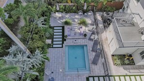 A rooftop pool area with a rectangular pool, surrounded by potted plants, outdoor furniture, and a metal railing. - Chic Studio Steps to Fort Lauderdale Beach! (Fort Lauderdale)