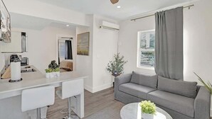 Ett modernt vardagsrum med en grå soffa, ett soffbord och en matplats med ett vitt bord och stolar.