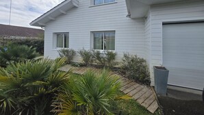 Een wit huis met twee verdiepingen, een garage, omgeven door een houten terras en verschillende planten.