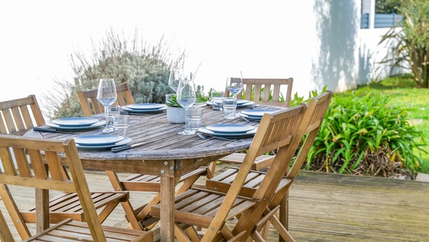 Una mesa redonda de madera al aire libre con sillas, platos y vasos.