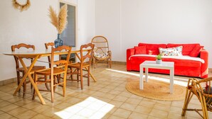 Una sala de estar con sofá rojo, sillas de madera, una mesa de comedor y un jarrón con plumas de pampa.