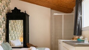 Un dormitorio con cama, techo de madera, baño con ducha y ventana.