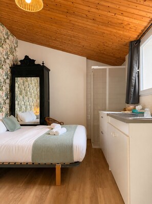 Une chambre avec un lit, un plafond en bois, une salle de bain avec douche et une fenêtre.