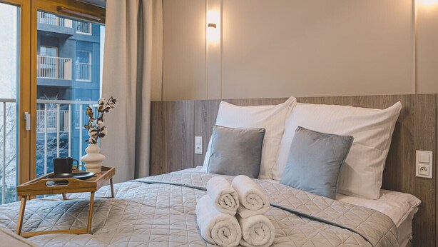Een hotelkamer met een bed, een nachtkastje met een vaas en uitzicht op een gebouw.