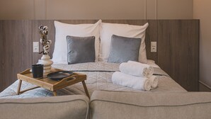 Een keurig opgemaakt bed met een houten hoofdbord, een nachtkastje met dienblad en een vaas met gedroogde bloemen.