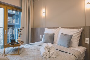 A hotel room with a bed, a bedside table with a vase, and a view of a building outside. - Studio in Nowy Port | Center | Opera Nova | Wi-Fi (Bydgoszcz)