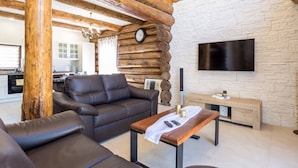 A modern living room with a leather sofa, wooden beams, a stone wall, and a flat-screen TV. - Holiday Home Elizabeta (Slunj)
