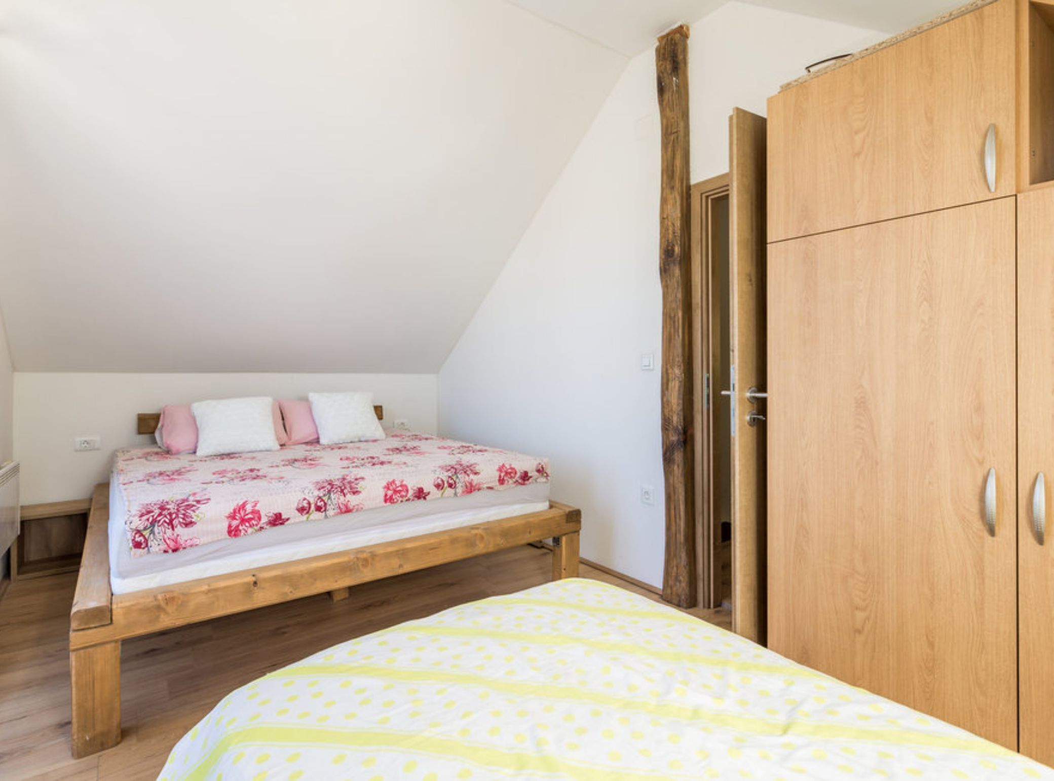 Ein Schlafzimmer mit einem Bettgestell aus Holz, einem großen Kleiderschrank und einer schrägen Decke.