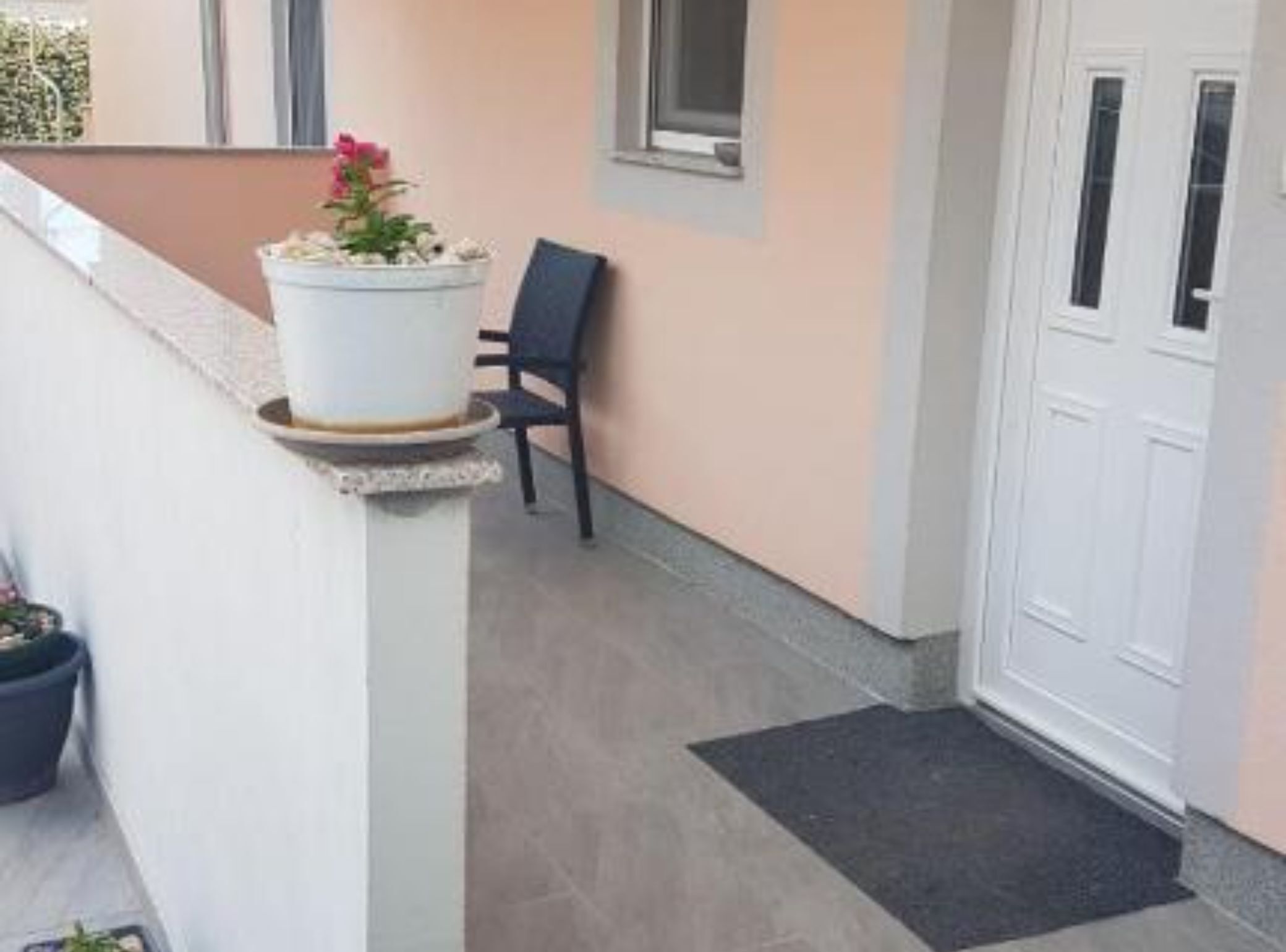 Un balcone con una pianta in vaso, una sedia e una porta bianca.
