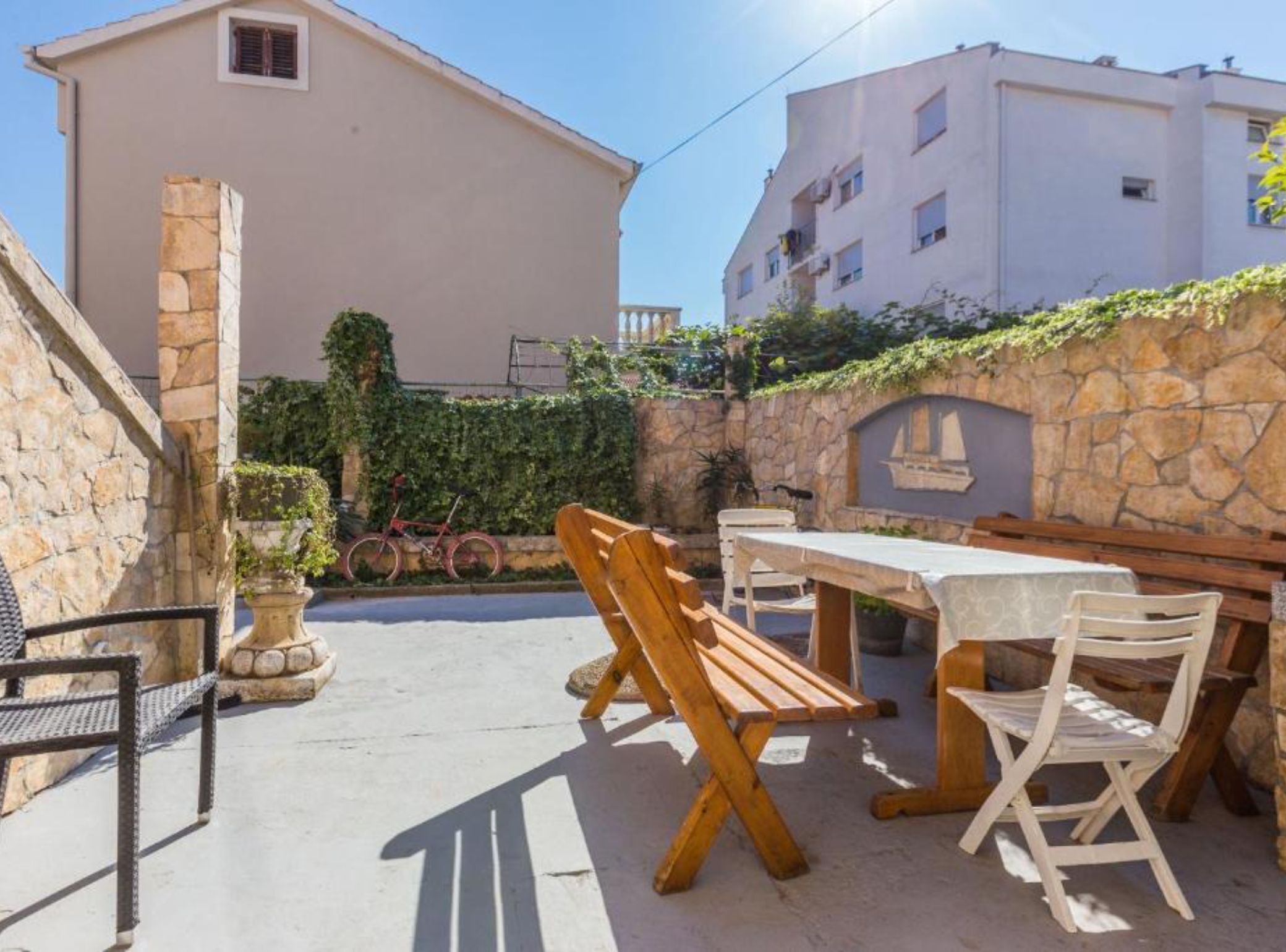 Eine Außenpatio mit Holztisch und -stühlen, einer Steinmauer mit Pflanzen und einem Gebäude im Hintergrund.