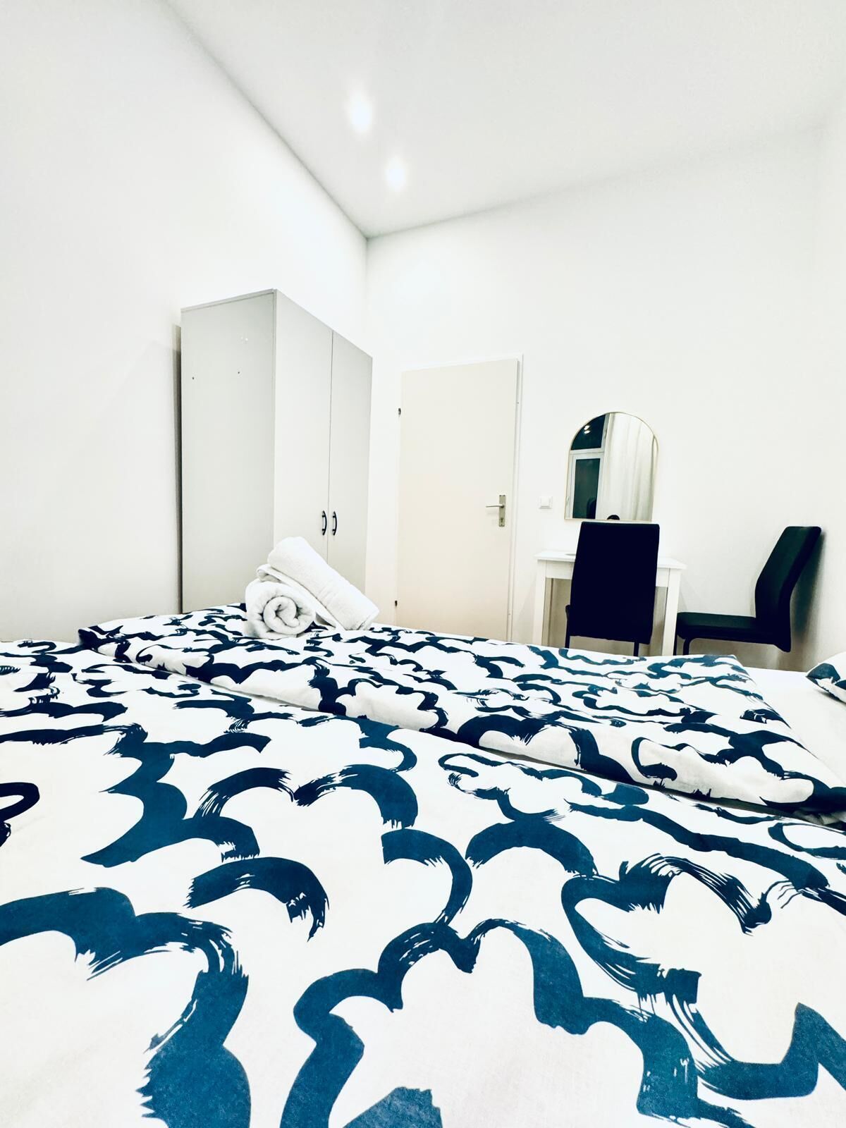 A hotel room with a bed, a wardrobe, a desk, and a chair.