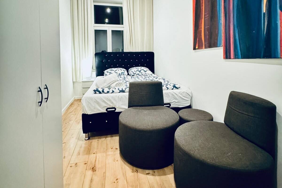 Une chambre avec un plafond en bois, un lit recouvert d’une literie à motifs, deux poufs et des œuvres d’art abstraites accrochées au mur.