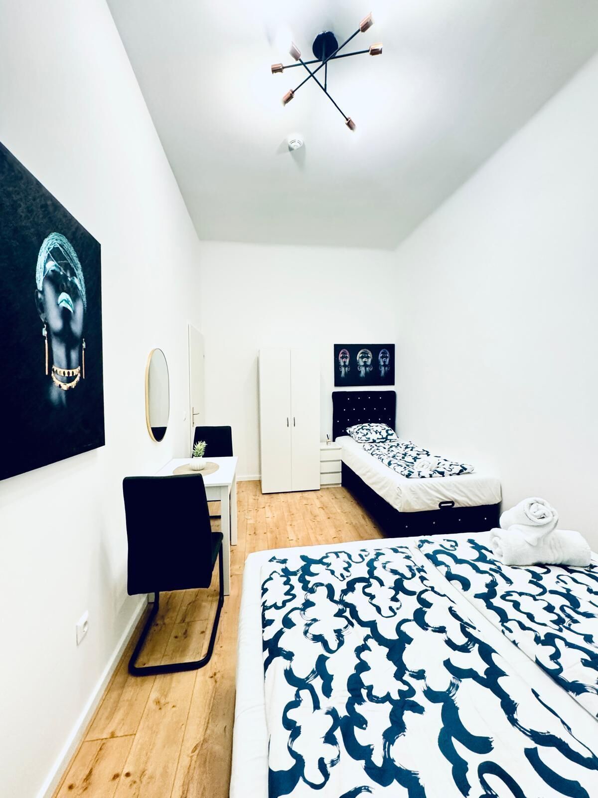 A modern bedroom with a bed, a desk, a wardrobe, and a ceiling light fixture.