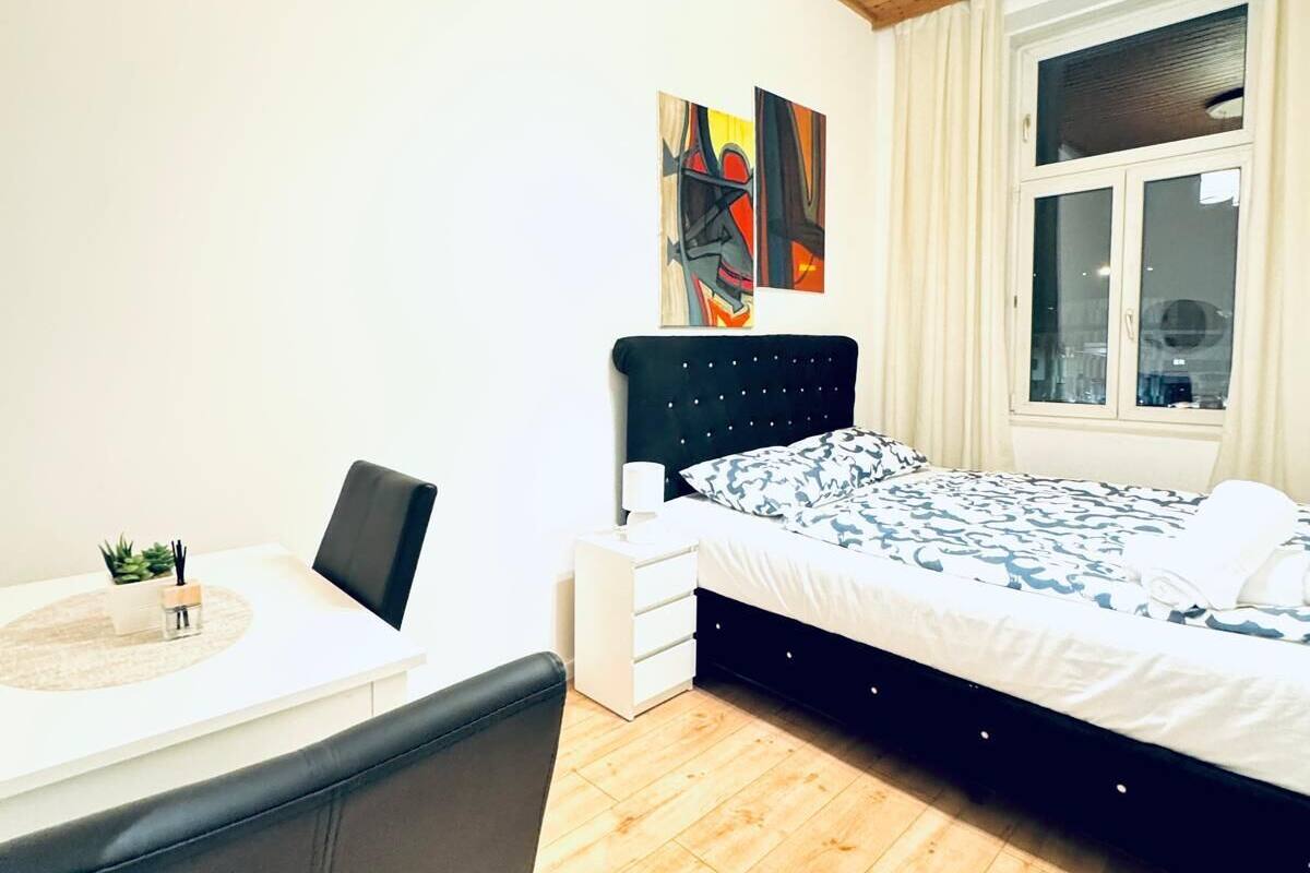 Une chambre moderne avec un plafond en bois, un lit doté d’une tête de lit noire, une table de chevet avec une lampe et une fenêtre avec des rideaux.
