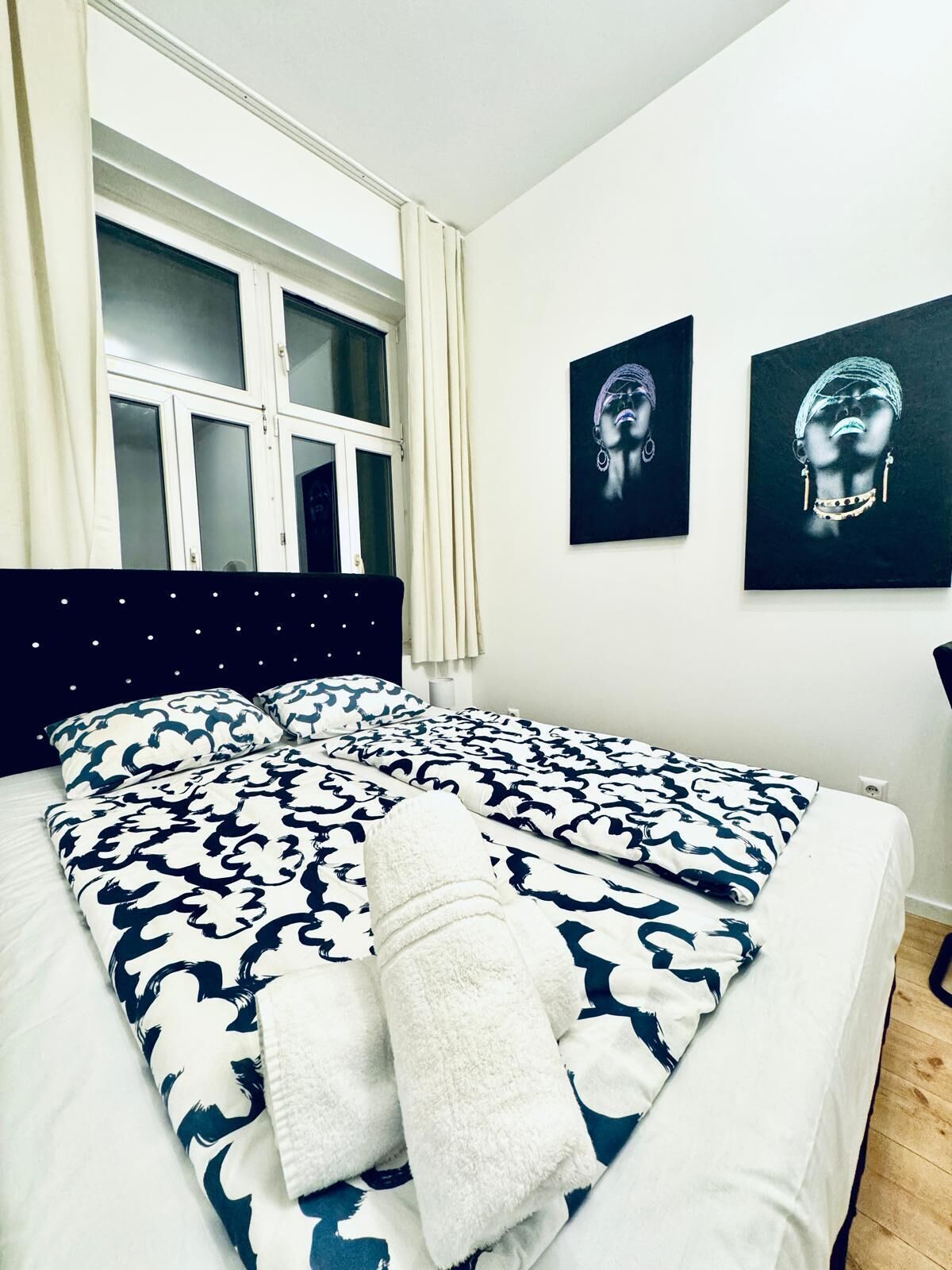 A bedroom with a bed, a window, and two wall-mounted artworks.