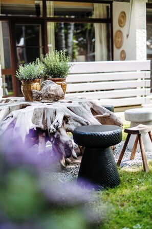 A rustic outdoor seating area with a wooden table, two potted plants, and a stone bench. - Das Esel - Kleinod in Rust (Rust)