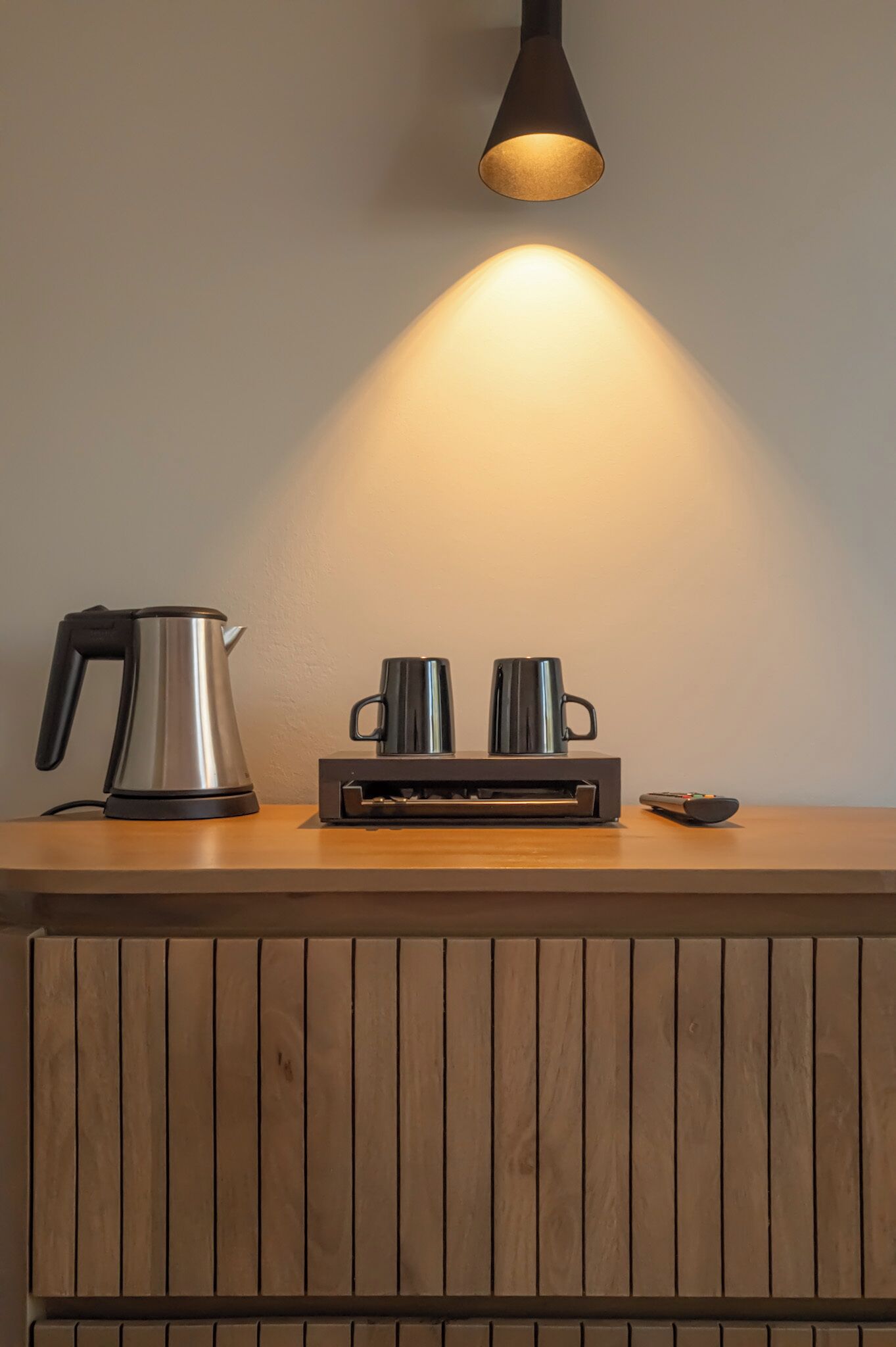 Una mesa de madera con una tetera, dos tazas, una impresora y un control remoto.