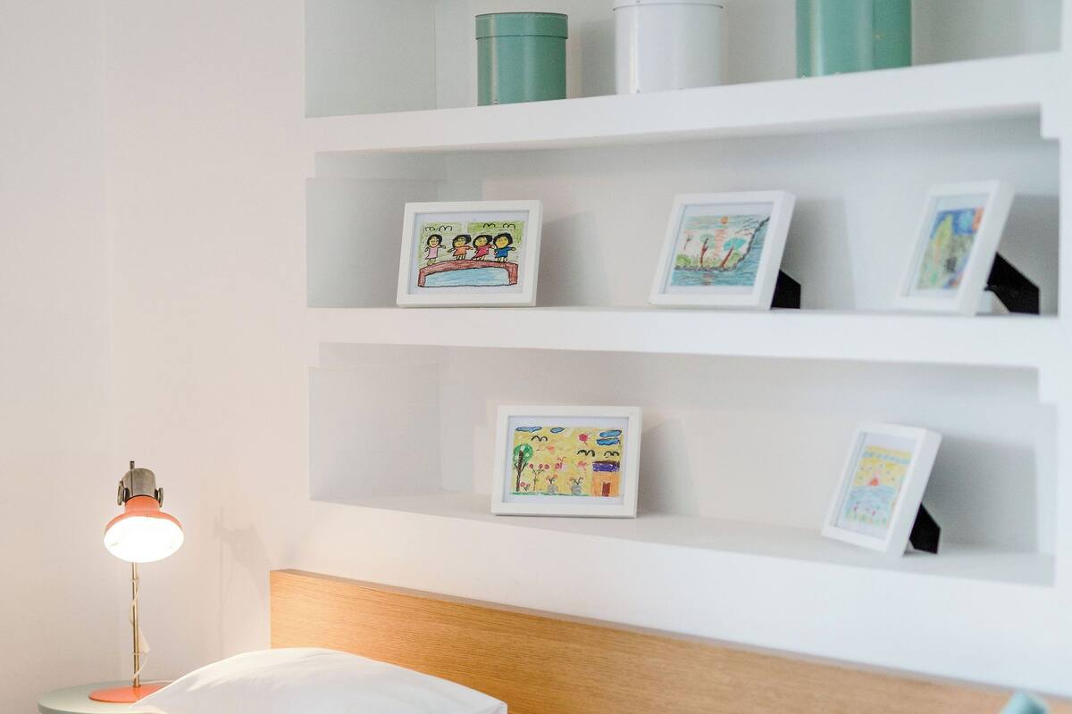 Quarto bem arrumado com cabeceira de madeira, luminária de cabeceira e prateleiras com quadros e recipientes.