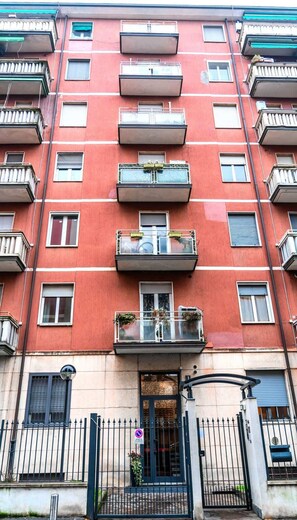 A multi-story residential building with balconies, a gated entrance, and a door with a window.