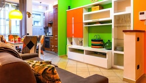 A living room with a sofa, a dining table with chairs, a kitchen area with cabinets, and a bright green accent wall.