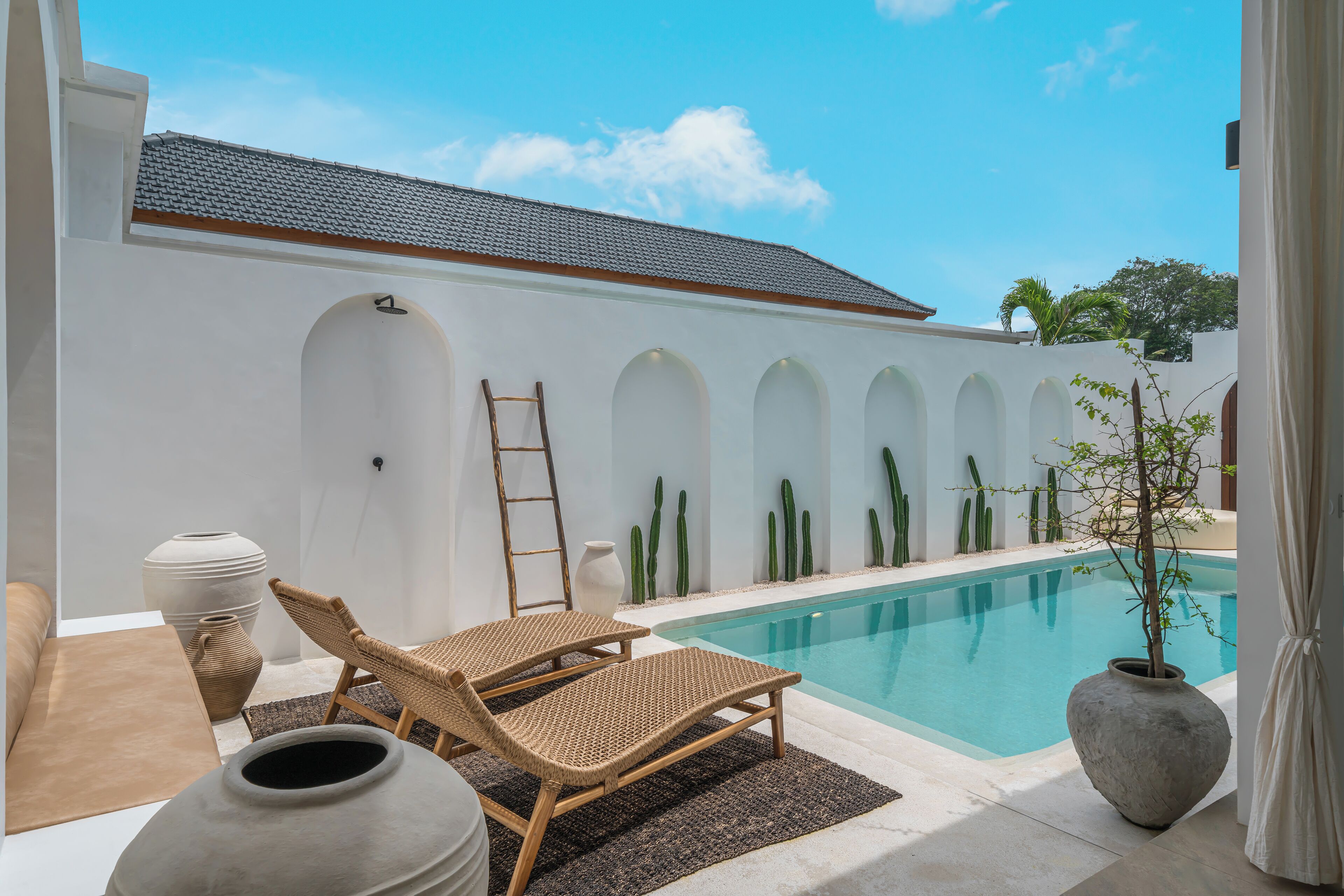 A poolside area with a white building, two wicker lounge chairs, a large vase, and a potted plant.