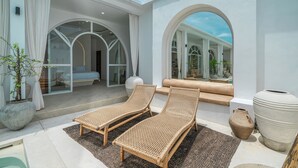 A modern outdoor lounge area with two wicker lounge chairs, a large potted plant, and a stone vase. - Villa Halle (Cemagi)