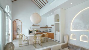 A modern kitchen with white cabinets, a dining area with gold chairs, and a large pendant light. - Villa Halle (Cemagi)