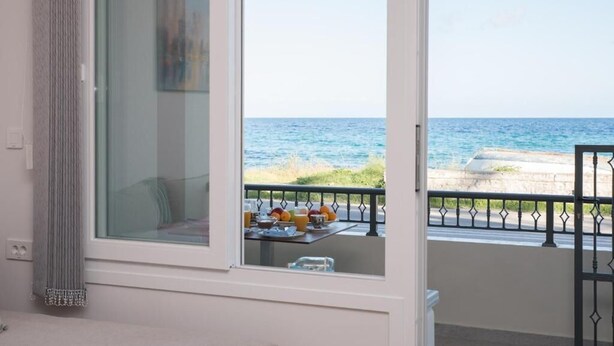 A room with a large window overlooking the sea, a balcony with a table set for breakfast, and a view of the coastline. - Sea n City  (Zakynthos)