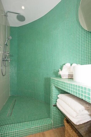 Een badkamer met groene betegelde wanden, een douchegedeelte en een handdoekhouder met opgevouwen handdoeken.