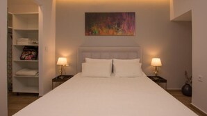 A neatly arranged bedroom with a large bed, two bedside tables with lamps, a closet with folded towels, and a colorful abstract painting on the wall. - Sea n City  (Zakynthos)