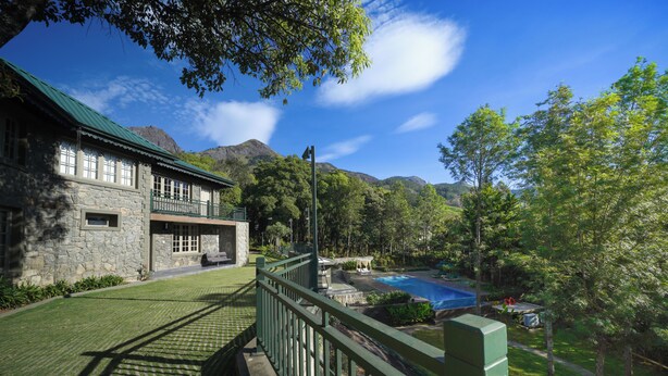 A stone building with a green roof, a pool, and a mountain backdrop. - The Farside Munnar (Devikolam)