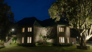 A stone building with a green roof, surrounded by a well-maintained garden and a large tree. - The Farside Munnar (Devikolam)