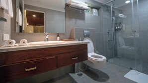 A modern bathroom with a glass-enclosed shower, a wooden vanity with a sink, and a toilet. - The Farside Munnar (Devikolam)