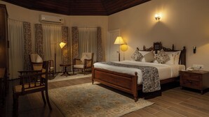 A bedroom with a wooden bed, two bedside lamps, a nightstand, a chair, a desk, and an air conditioning unit. - The Farside Munnar (Devikolam)