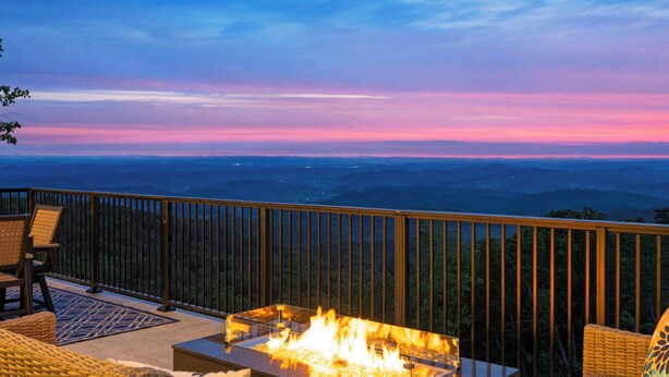 Une terrasse dotée d’un foyer, de meubles en osier et offrant une vue sur les montagnes lointaines.