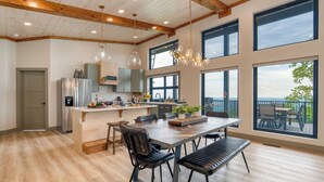 Une cuisine spacieuse dotée d’un grand îlot central, de poutres apparentes en bois au plafond et de grandes fenêtres offrant une vue sur l’extérieur.