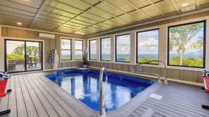 Une piscine dotée d’une terrasse en bois, de grandes fenêtres et offrant une vue sur le paysage.