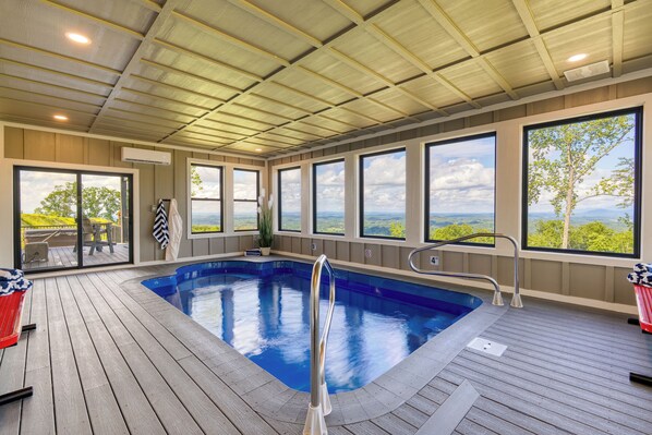 Une piscine dotée d’une terrasse en bois, de grandes fenêtres et offrant une vue sur le paysage.