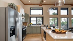 Une cuisine moderne dotée d’un réfrigérateur en acier inoxydable, de meubles en bois et d’une grande fenêtre donnant sur un balcon.