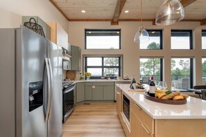 Une cuisine moderne dotée d’un réfrigérateur en acier inoxydable, de meubles en bois et d’une grande fenêtre donnant sur un balcon.