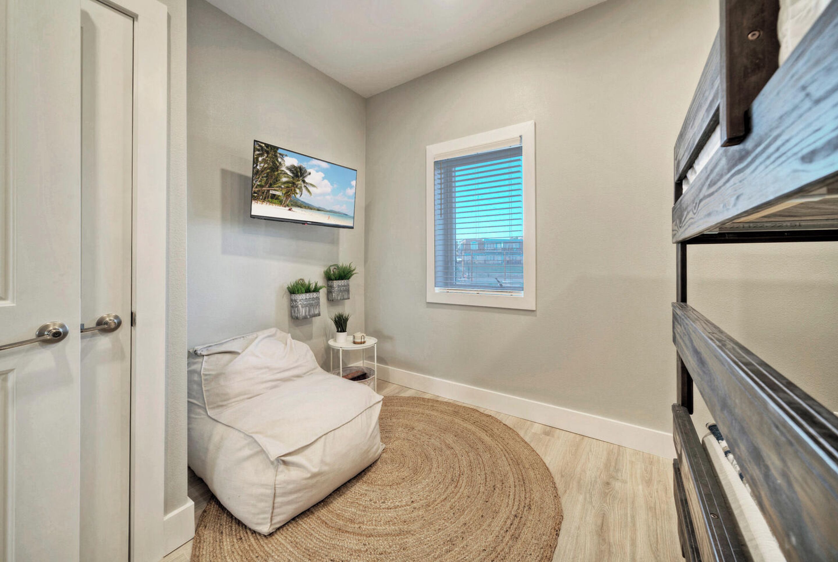 A bedroom with a bed, a small bedside table, a window with blinds, and a picture on the wall.
