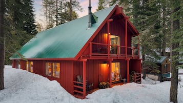 Une cabane rouge, surmontée d’un toit vert, entourée de neige et nichée au cœur d’une forêt.