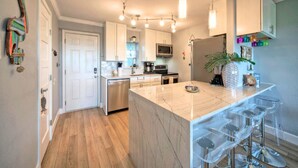 A modern kitchen with a marble island, bar stools, stainless steel appliances, and a hanging light fixture.