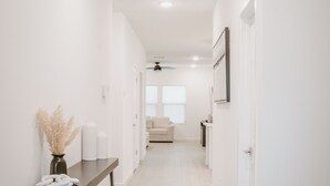 Un pasillo moderno con piso de madera, paredes blancas y un ventilador de techo.